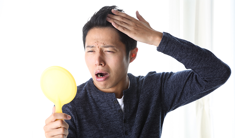 鏡を見て、生え際を気にする男性