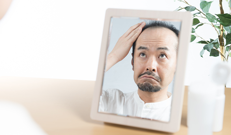 鏡を見て、薄くなった頭髪を気にする男性