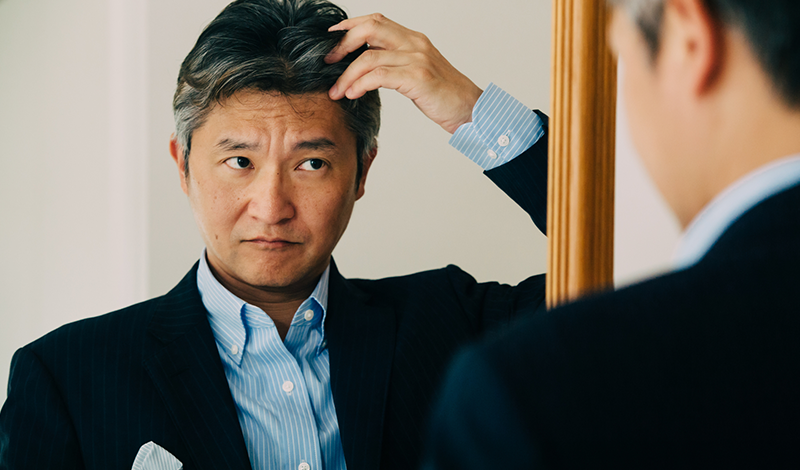 鏡で自分の生え際を確認する男性