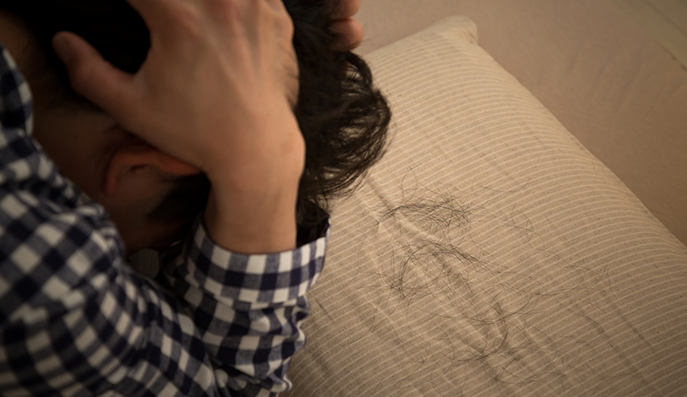 枕に落ちている抜け毛をみて、落ち込む男性