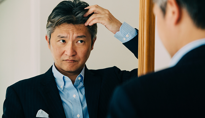 鏡で自分の生え際を確認する男性
