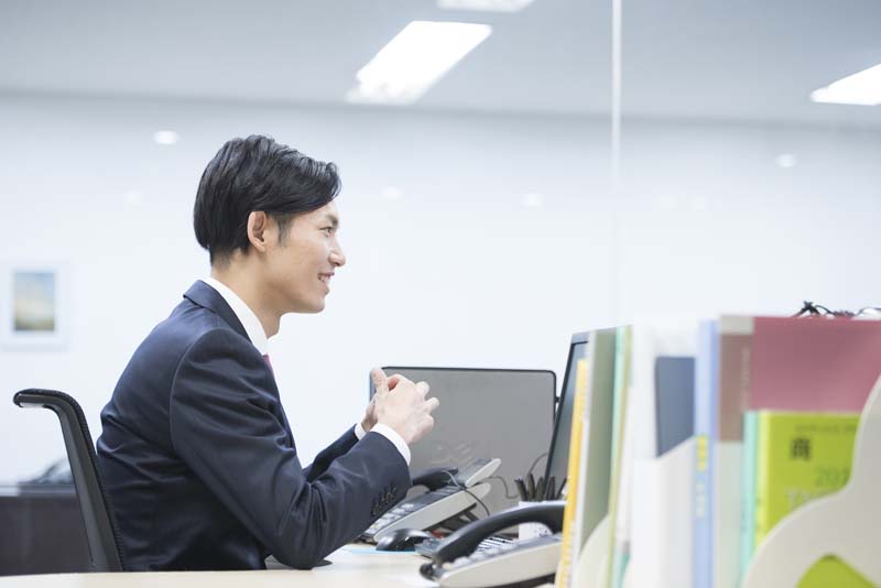 オフィスの自席でほほ笑む男子絵