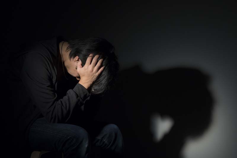 頭を抱え暗い部屋で悩む男性