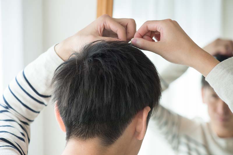 鏡を見て自分の髪の毛先を気にする男性