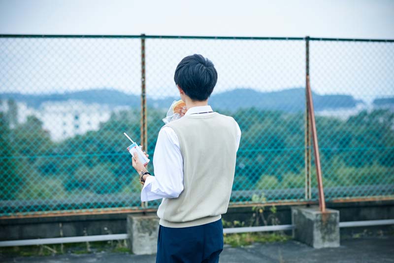 屋上でパンをかじる学生