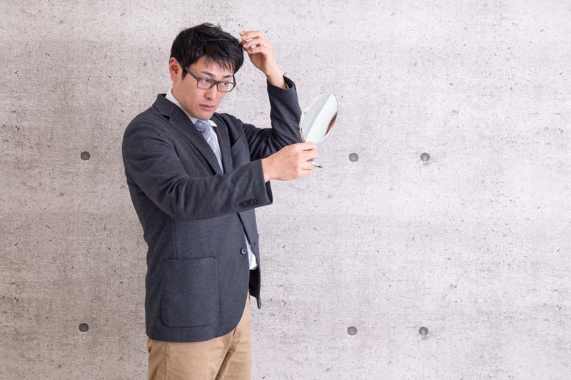 手鏡をのぞき込みながらヘアスタイルを整えている男性