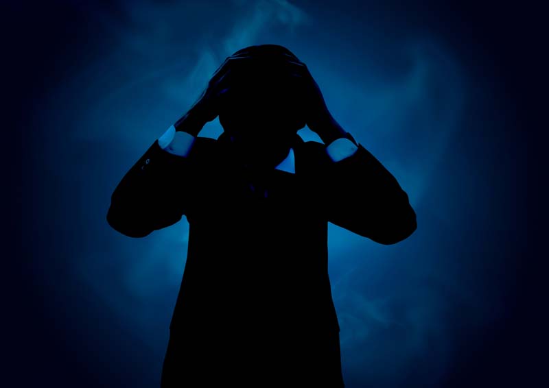 背後から迫る過剰なストレスに頭を抱える男性