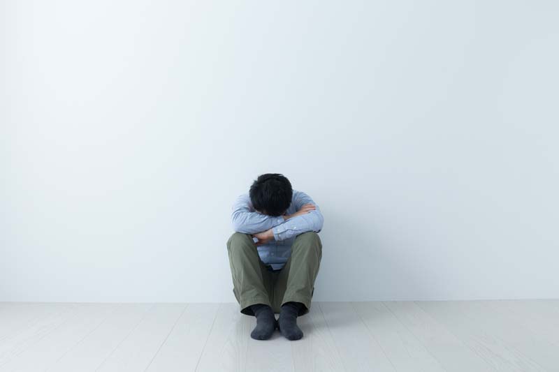 膝を抱えてうなだれる男性