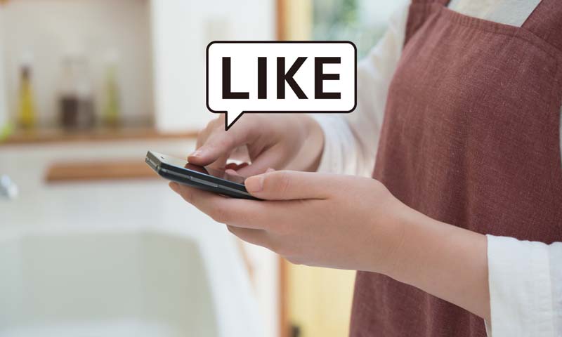 女性が携帯でSNS「LIKE」を押す写真