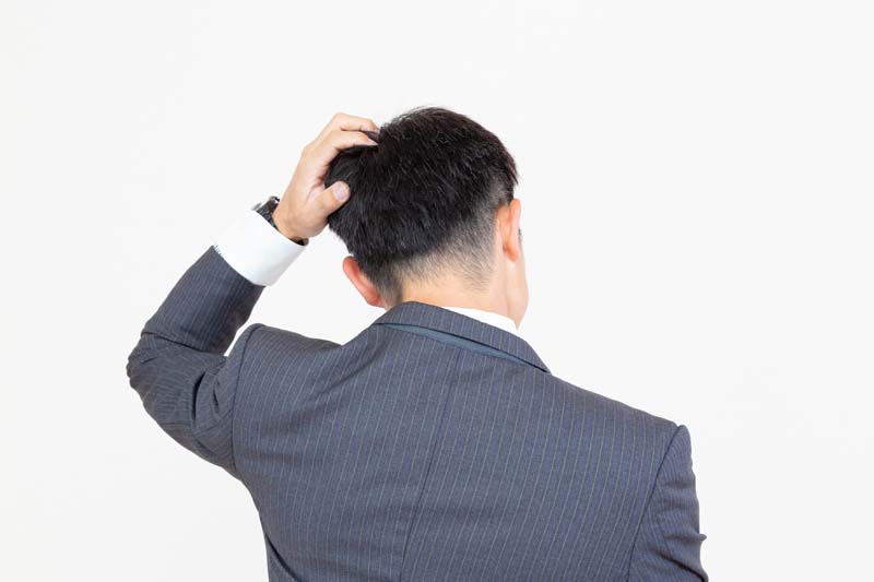 つむじあたりを手で押さえる男性の後ろ姿