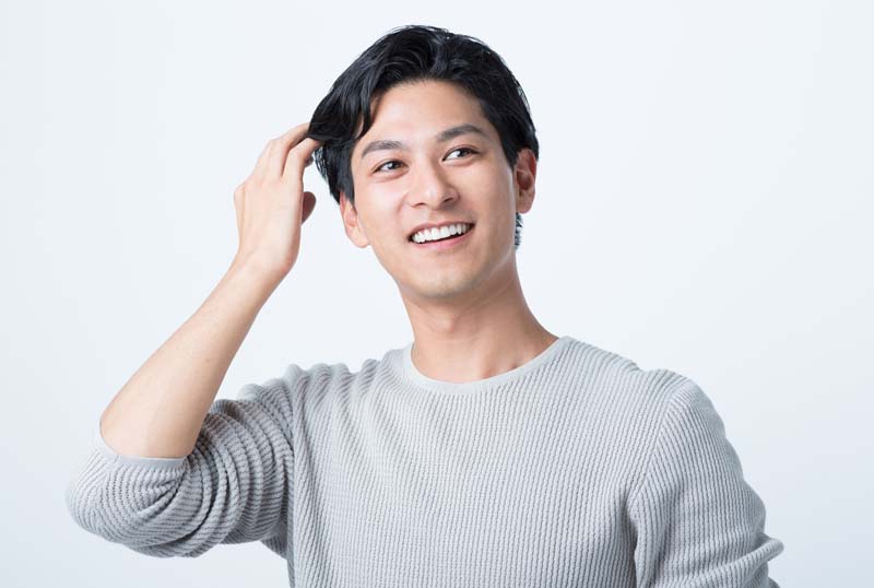 笑顔で髪の毛を触る男性の姿