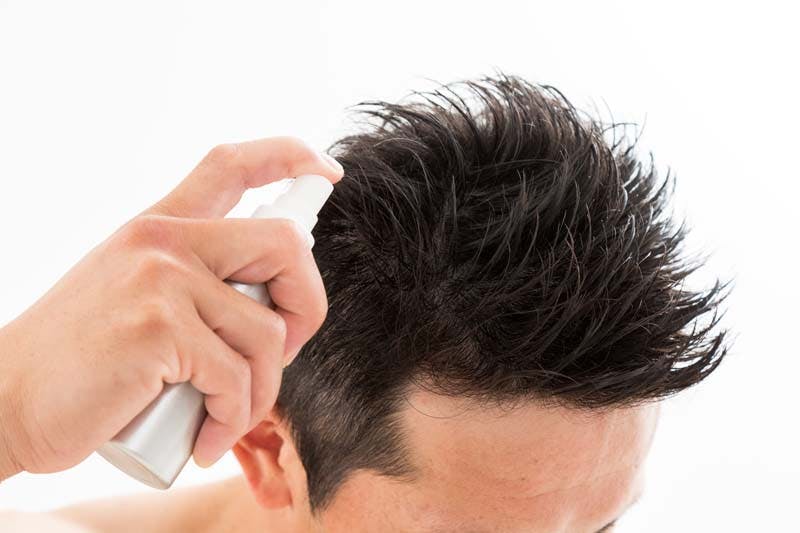 男性が頭髪に増毛スプレーをする様子