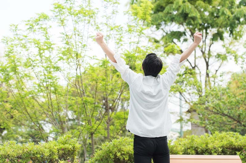 白い服を着た男性が自然の中で伸びをしている様子