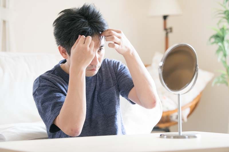 鏡で髪型をチェックする男性画像