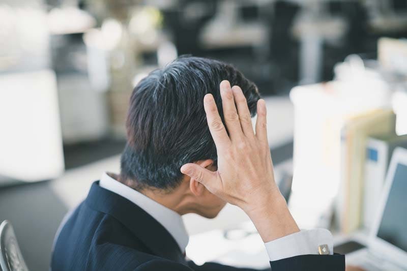 側頭部に手を当ててカツラ(ウィッグ)のズレを気にしている男性のイメージ画像