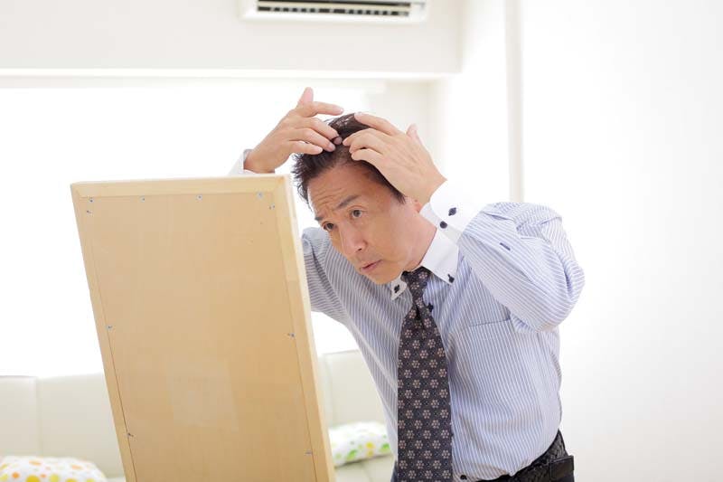 鏡を覗き込みながら生え際を気にする旦那さんのイメージ画像
