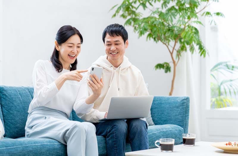 スマートフォンを見ながら会話する旦那さん・奥さまのイメージ画像