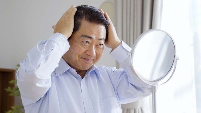 髪の毛に手を当てて身だしなみを整えている男性のイメージ画像