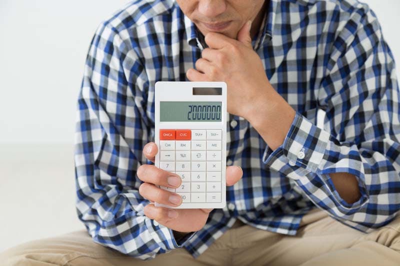 電卓を手に取ってお金の勘定をしている男性のイメージ画像