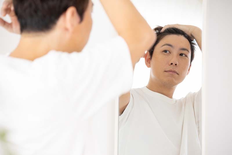 鏡を見て生え際をチェックする男性のイメージ画像