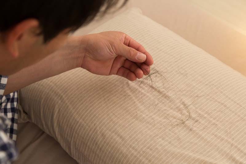 枕についた抜け毛を気にする男性のイメージ画像