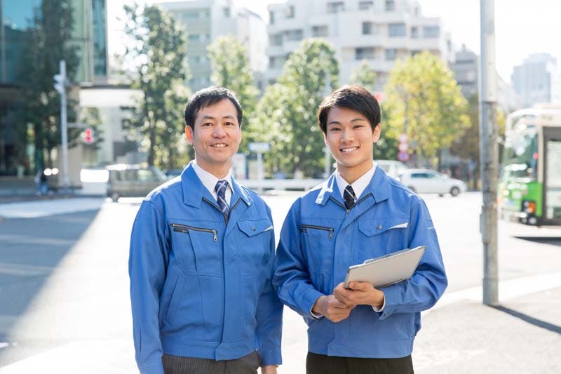 職場の後輩と笑顔で並ぶ男性のイメージ画像