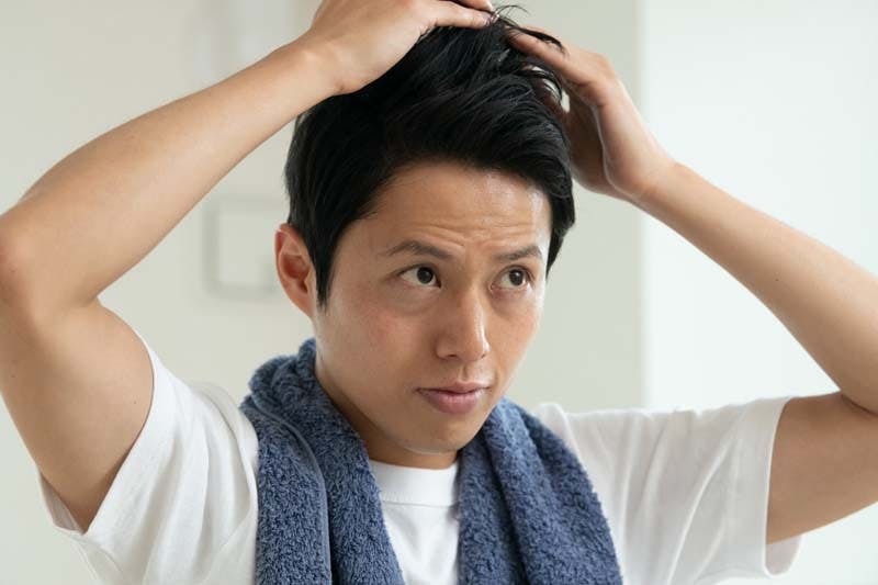 寝癖を気にして髪の毛を触る男性のイメージ画像