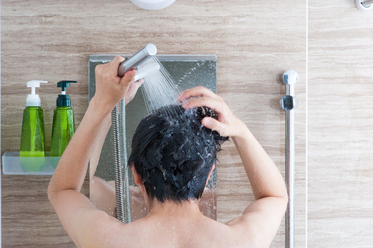 シャンプーの泡を洗い流している男性のイメージ画像