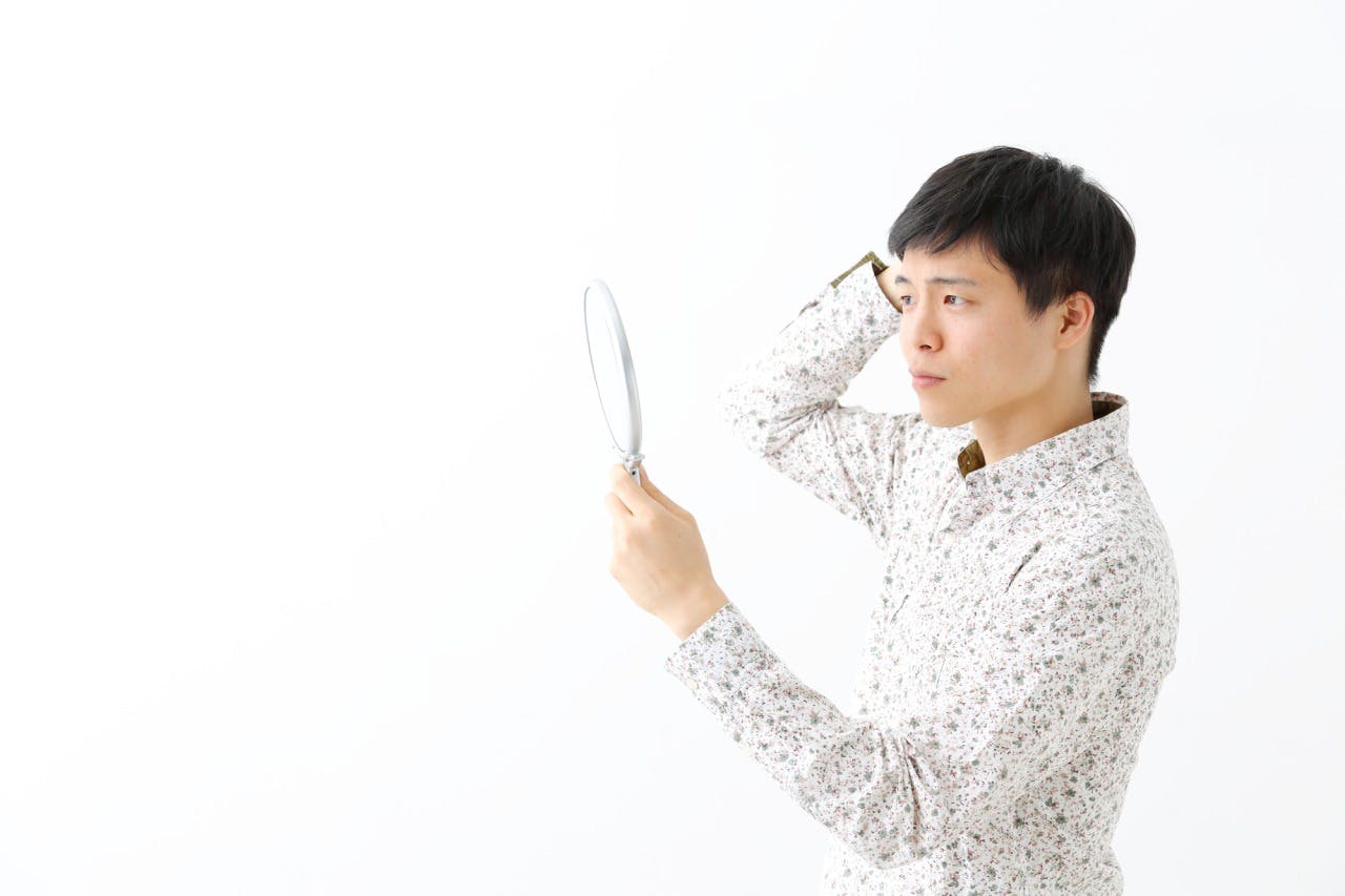 髪の毛を気にする、手鏡を持った若い男性