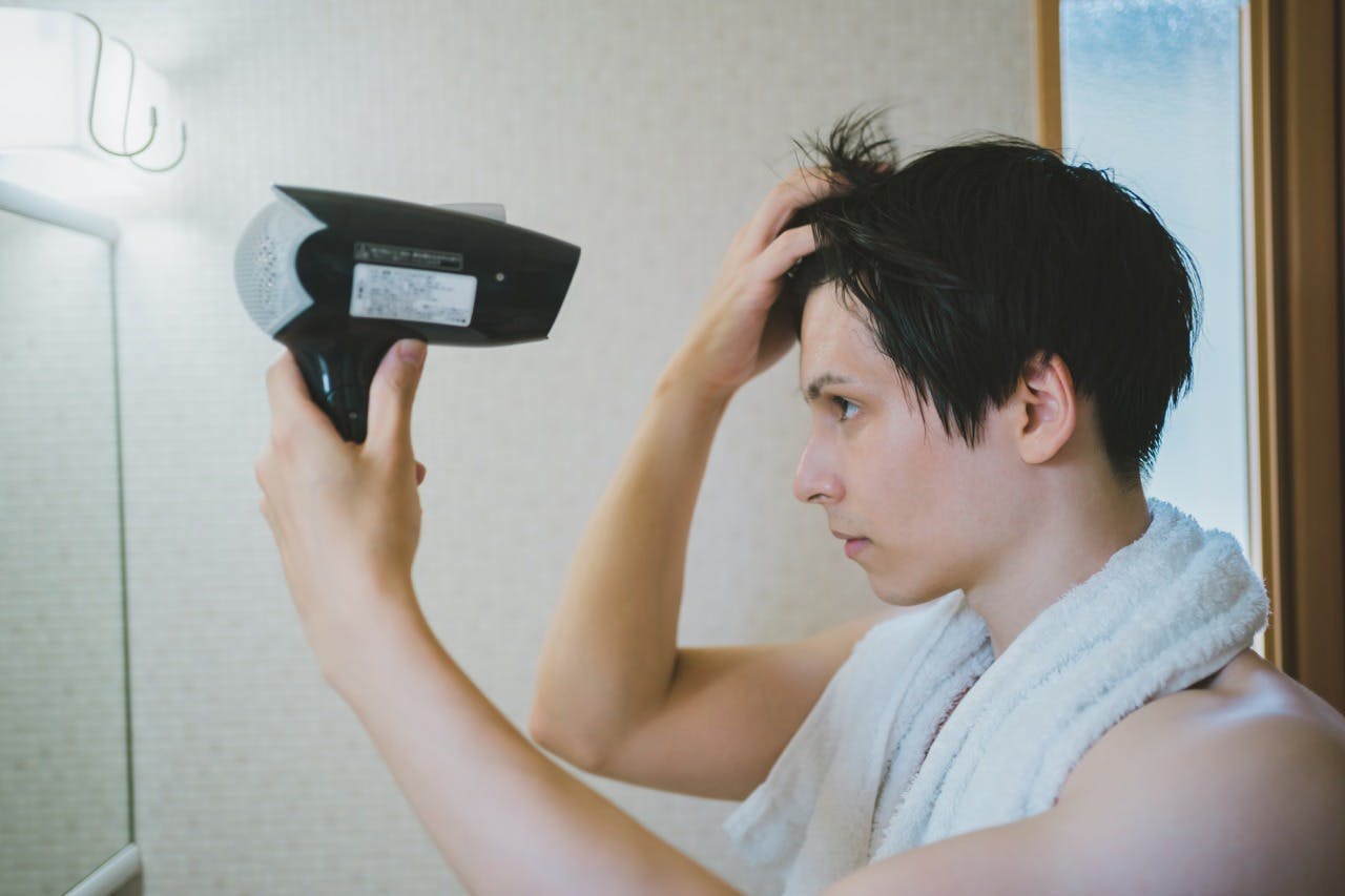 洗面台でドライヤーを使って髪を乾かしている男性のイメージ画像