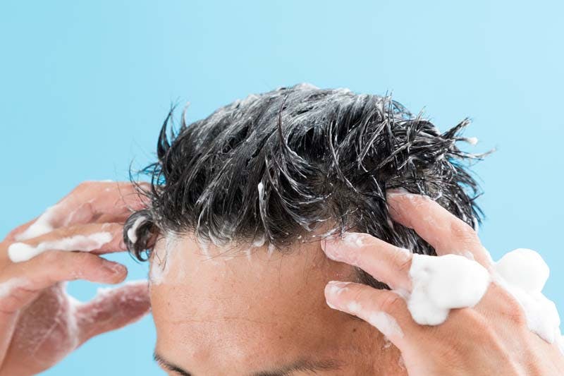 シャンプーを泡立てて洗髪する男性のイメージ画像