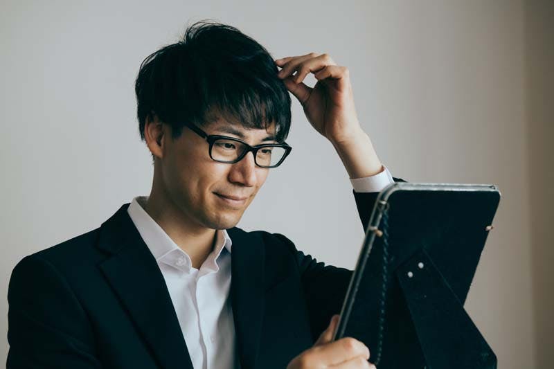 鏡を手に持って髪型を調整する男性のイメージ画像