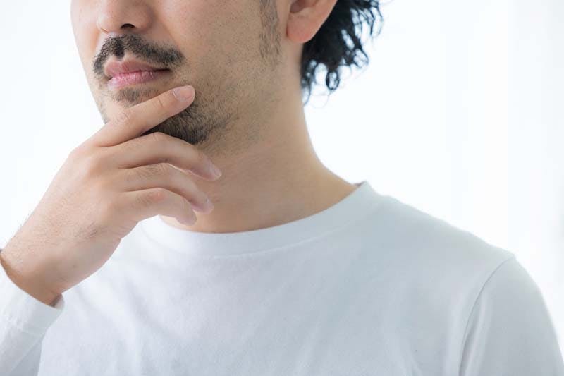 髭に手を当てて脱毛を考える男性の画像