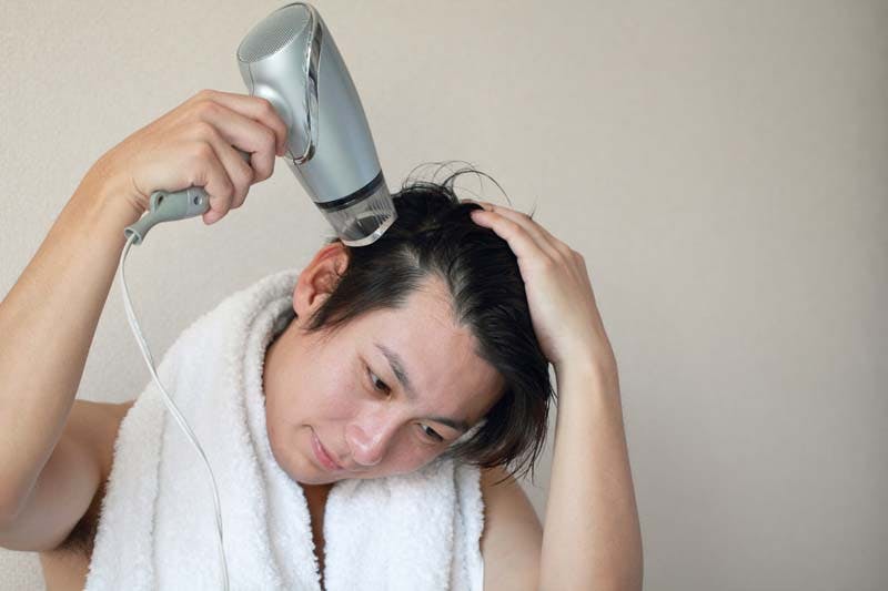 ドライヤーで髪を乾かす男性の画像