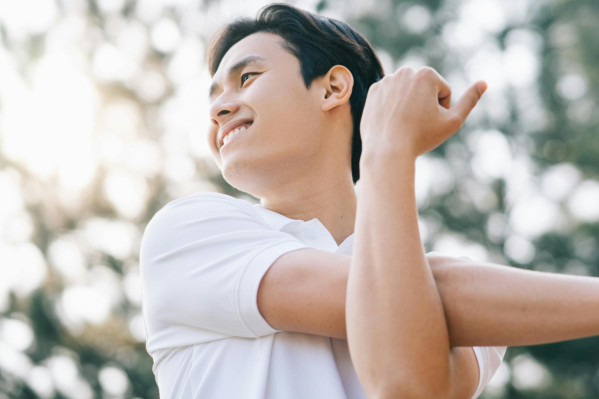 晴天下、木々をバックに胸の前で腕をクロスする笑顔の男性のアップ