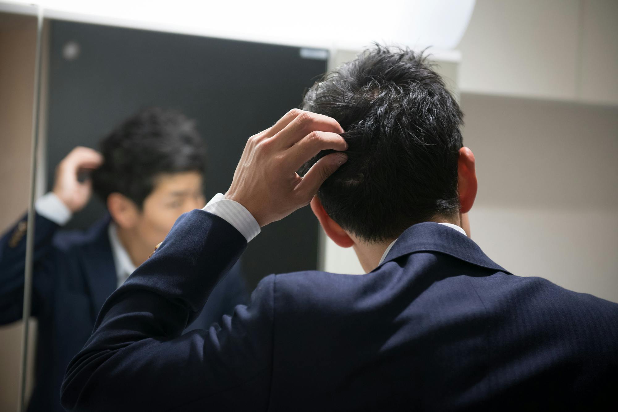 鏡に向かってヘアワックスのついた後頭部をセットする男性ビジネスパーソン