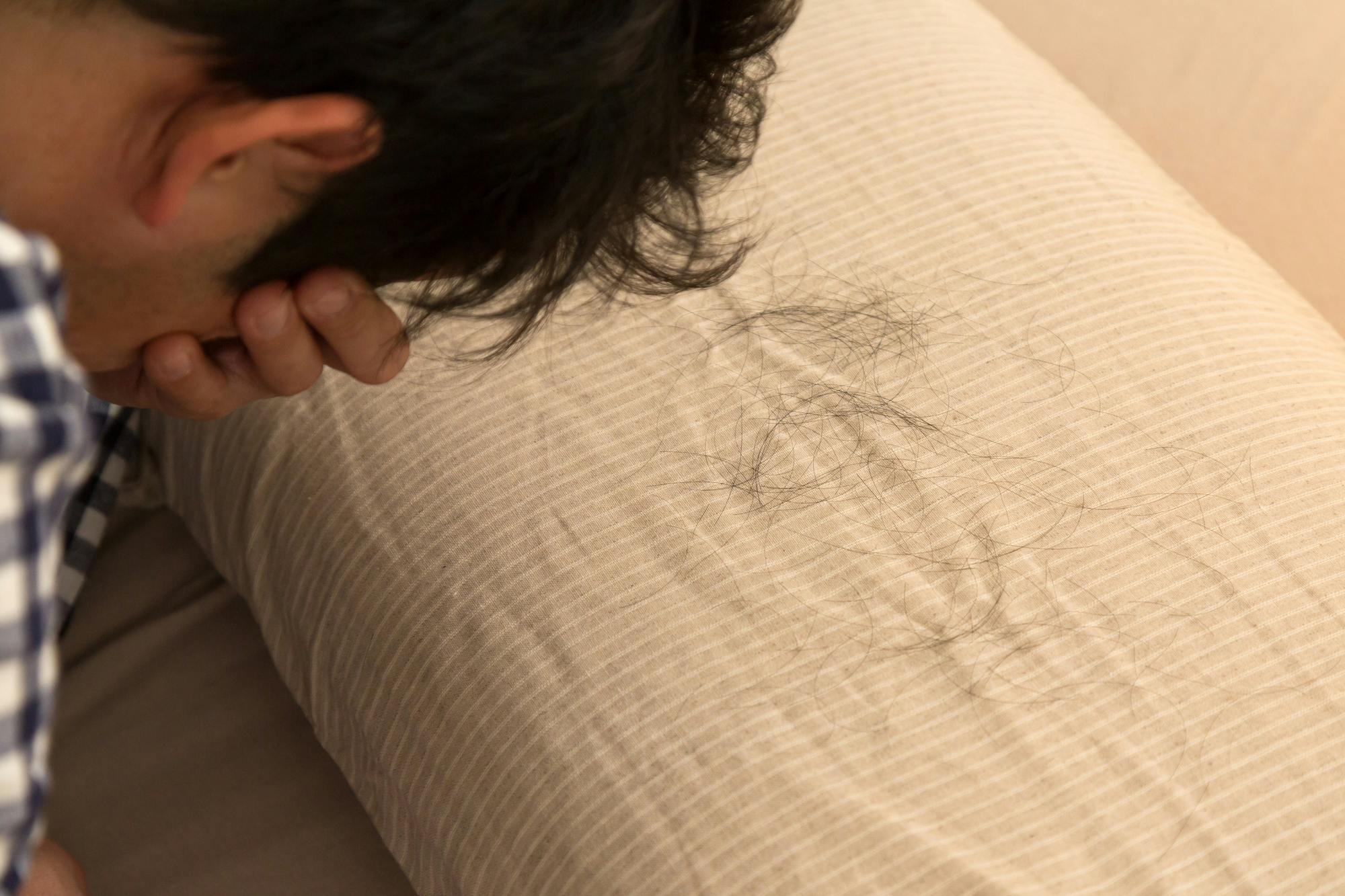 枕に付いた多数の抜け毛を見てうなだれる男性