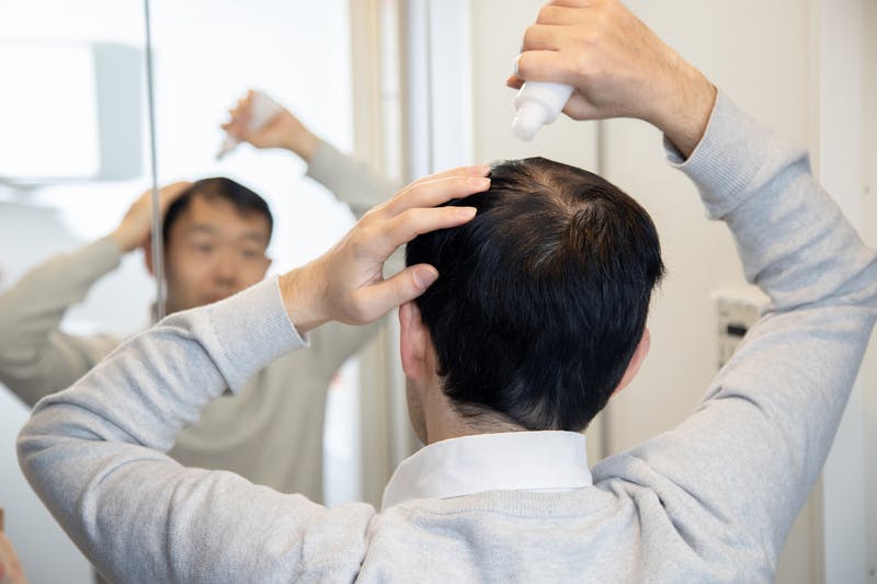 三面鏡を前に育毛剤を使う男性