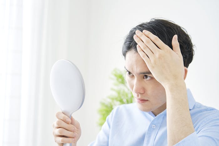 手鏡を見て額をチェックしている男