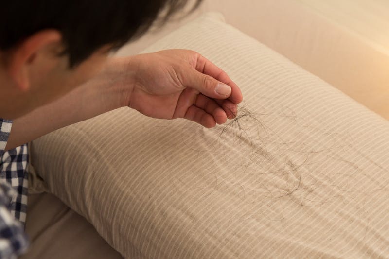 枕の上に落ちた抜け毛を確認している男性
