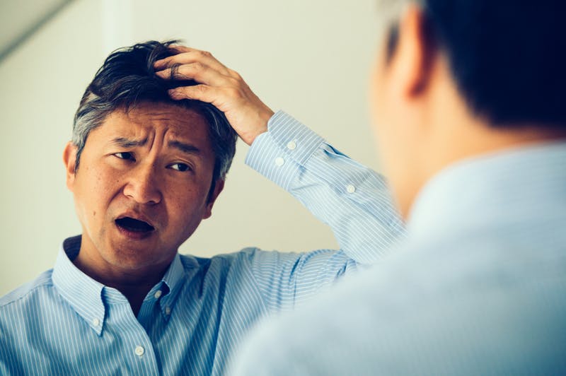 鏡で自身をチェックし髪を触る男性