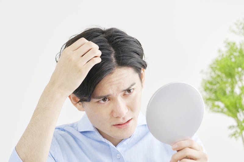 手鏡で頭皮をチェックする男性