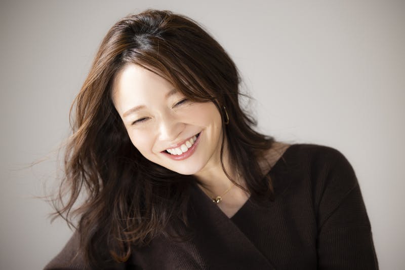 うつむき加減で微笑むロングヘアの女性