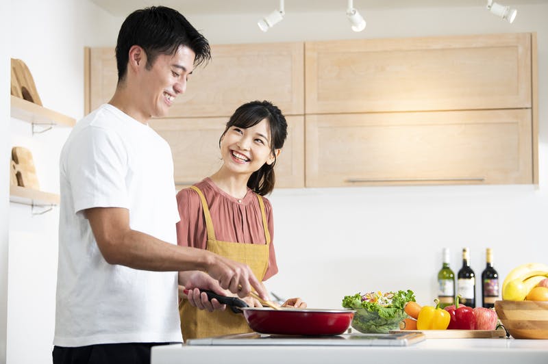 明るいキッチンで料理をする男性に笑顔で話しかける女性