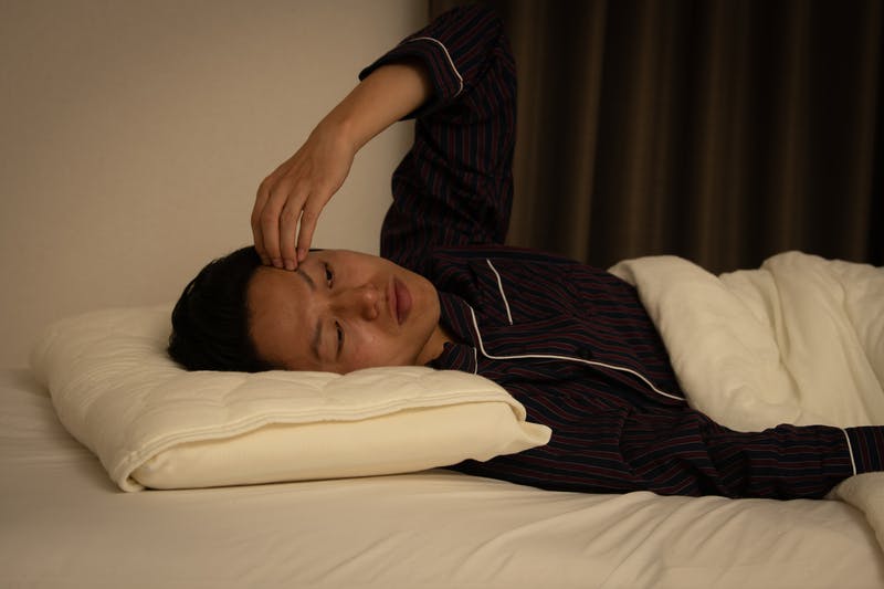 ベッドで寝ながら悩んでいる1人の男性