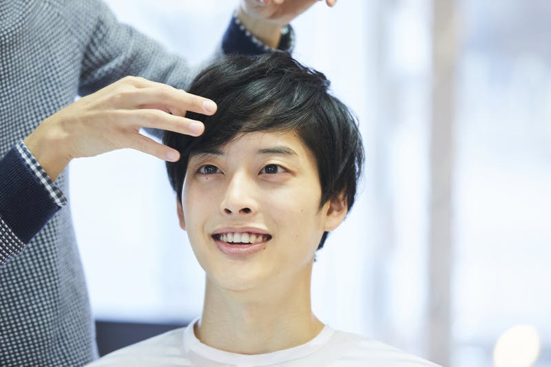 ヘアメイクを受け笑顔で仕上がりを確認する若い男性
