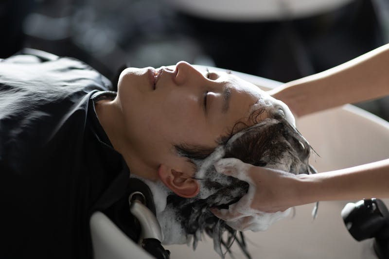 ヘアサロンで心地よさそうにシャンプーをしてもらう若い男性