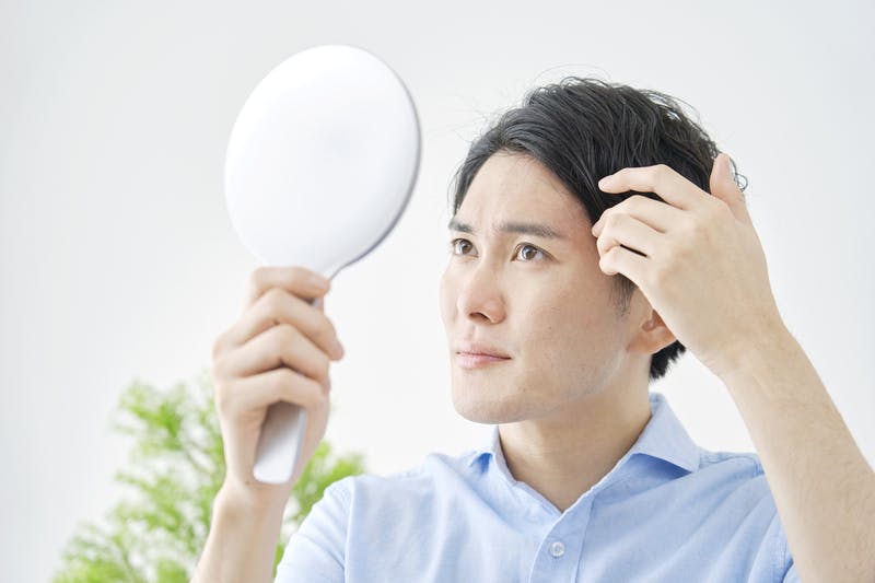 手鏡で生え際の髪をチェックする男性