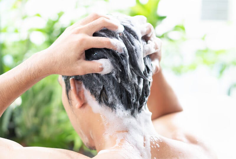 頭部をつかむようにしてシャンプーで洗髪する男性