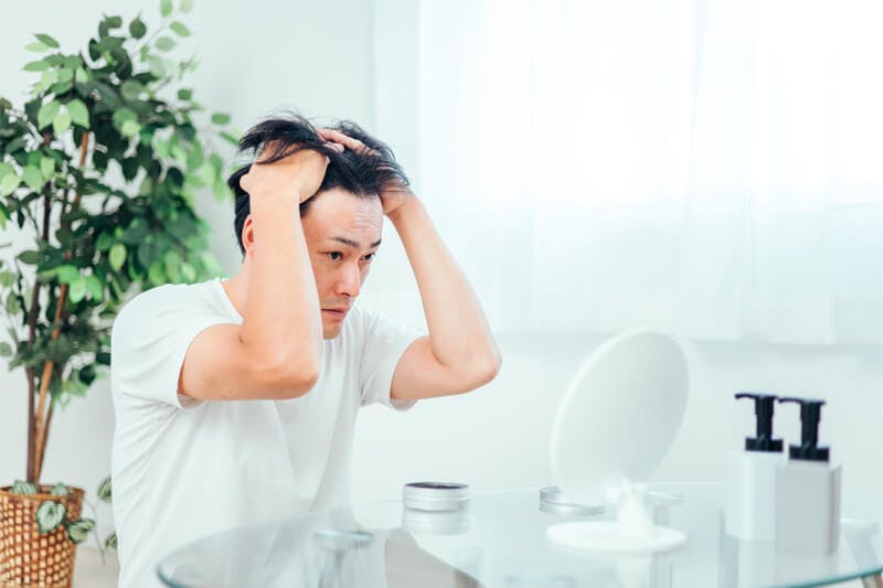 整髪料を手に取り、髪をかき上げて塗り込む男性整髪料を手に取り、髪をかき上げて塗り込む男性